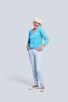 Trendy grandmother. Full length of beautiful senior woman looking at camera and smiling while standing against grey background