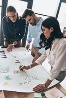 Team of innovators. Top view of young confident business people discussing something while working with blueprint in the office photo
