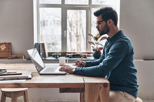 Developing new project. Side view of concentrated young man using computer while working in the office photo