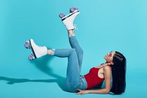 Attractive young woman wearing roller skates and smiling while lying against blue background photo