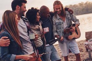 Best place to rest. Group of young people in casual wear smiling while enjoying beach party near the lake photo