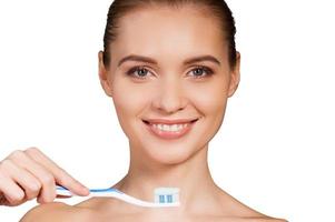 mujer cepillándose los dientes. hermosa joven sosteniendo cepillo de dientes con pasta de dientes y sonriendo a la cámara mientras está aislada en el fondo blanco foto