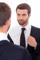 Confident in himself. Handsome young man wearing jacket and smiling while standing against mirror photo