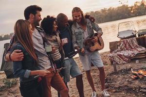 mejor lugar para descansar. grupo de jóvenes con ropa informal sonriendo mientras disfrutan de una fiesta en la playa cerca del lago foto