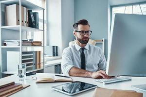 Modern young man in formalwear working using technologies while sitting in the office photo