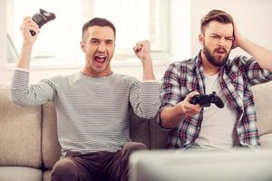 Friends and video games. Two handsome young men playing video games while sitting on sofa photo