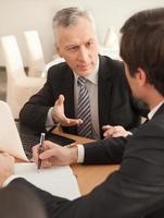 Finding a solution. Two business people in formalwear discussing something while sitting at the table photo