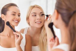 Doing make-up together. Two beautiful young women doing make-up together while looking at the mirror and smiling photo