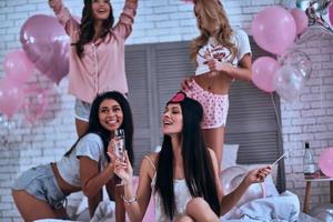 Leave all the worries behind. Four attractive young smiling women in pajamas drinking champagne while having a slumber party photo