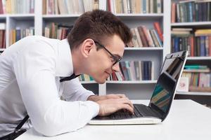 friki del ordenador. vista lateral del joven nerd con camisa y corbata de moño escribiendo algo en la computadora foto