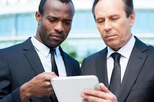 discutiendo un nuevo proyecto juntos. dos hombres de negocios confiados mirando la tableta digital mientras uno de ellos la señala con el dedo foto