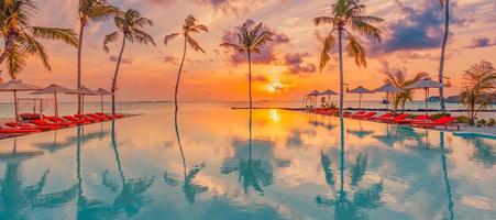 Luxury sunset over infinity pool in a summer beachfront hotel resort at beautiful tropical landscape. Tranquil beach holiday vacation background. Amazing island sunset beach view, palms swimming pool