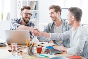 Sealing a deal. Business people shaking hands while sitting at the desk in office photo