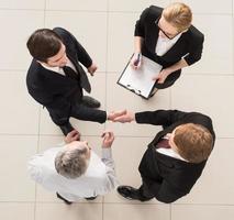 Business meeting. Top view of four people in formalwear standing close to each other while two of them handshaking photo