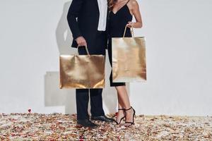 Close-up of fashionable couple carrying gold colored shopping bags while  standing against gray background photo