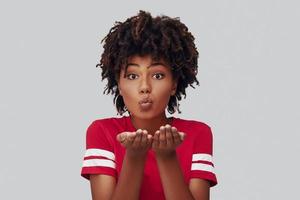 Attractive young African woman looking at camera and blowing a kiss while standing against grey background photo