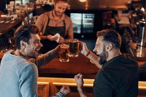 Top view of carefree young men in casual clothing drinking beer while sitting in the pub photo