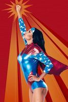 Going to save the world. Side view of beautiful young woman in superhero costume keeping arm outstretched while flying up against red background photo