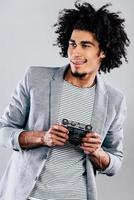 Cheerful photographer. Handsome young African man holding retro styled camera and looking away with smile while standing against grey background photo