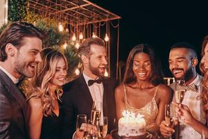 Group of people in formalwear holding birthday cake while spending time on party photo