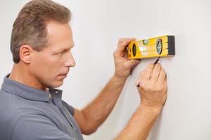 Taking wall measurements. Side view of confident mature man taking measurements of the wall photo