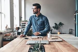 Taking some time to think. Thoughtful young man looking away while working in the creative working space photo