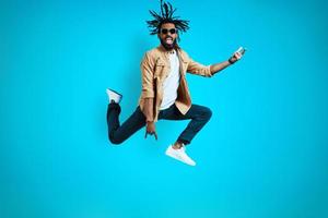 Full length of cheerful young African man in casual wear shouting and gesturing while hovering against blue background photo