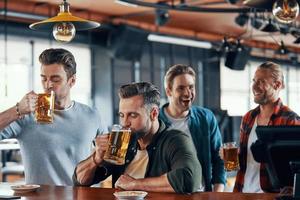 Group of handsome young men in casual clothing enjoying beer and communicating photo