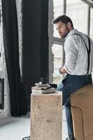 Irresistible man. Handsome young man in white shirt and suspenders looking away while leaning on sofa photo