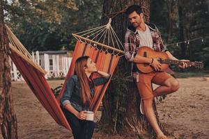 escuchando la canción del amor. un joven apuesto tocando la guitarra para su hermosa novia mientras pasa tiempo sin preocupaciones al aire libre foto