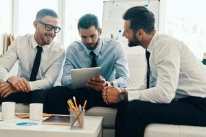 Brainstorming together. Group of young modern men in formalwear working using digital tablet while sitting in the office photo