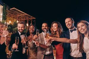 Group of people in formalwear toasting with champagne and smiling while spending time on luxury party photo