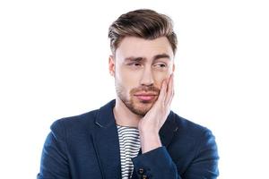 Feeling uncertain. Portrait of young man expressing uncertainty and looking away while standing against white background photo