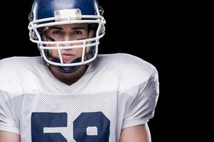 Strong and concentrated.  American football player looking at camera while standing against black background photo