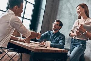 Young modern colleagues in smart casual wear shaking hands and smiling while working in office photo