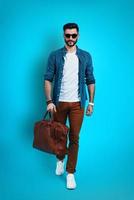 Full length of fashionable young man smiling and looking at camera while walking against blue background photo