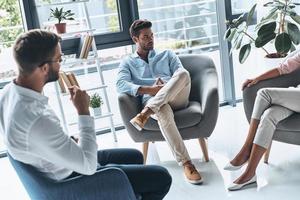 Listening his side of the story. Young married couple talking while sitting on the therapy session with psychologist photo