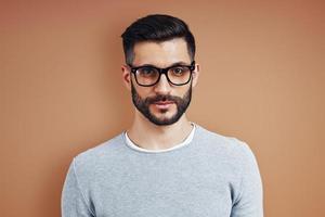 Charming young man in casual wear looking at camera while standing against brown background photo