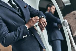 What time is it Close up of young man in full suit checking the time while standing in front of the mirror indoors photo