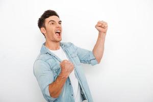 Real winner. Excited young man keeping arms raise and expressing positivity while standing against white background photo