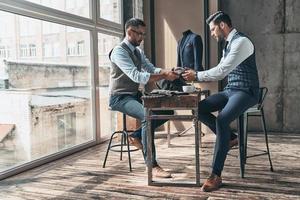 decisión difícil. joven diseñador de moda eligiendo tela con su cliente mientras se sienta en el taller foto