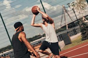 Showing his best shot. Two young men in sports clothing playing basketball while spending time outdoors photo