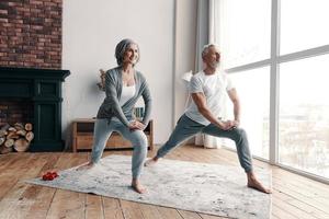 Good looking senior couple in sports clothing exercising and smiling while spending time at home photo