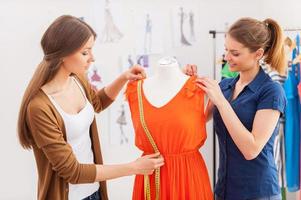 Working on new collection together. Two beautiful female designers measuring dress on the mannequin photo