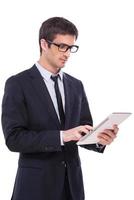 Businessman with digital tablet. Handsome young man in formalwear working on digital tablet while standing isolated on white background photo