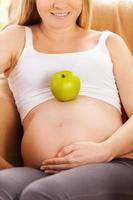 My baby will be healthy. Beautiful pregnant woman sitting on the chair while green apple laying on her belly photo