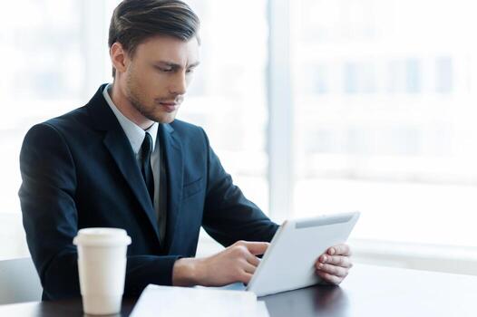 Internet user. Cheerful young man using digital tablet while coffee break in office photo