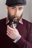 elegancia y masculinidad. retrato de un apuesto joven con sombrero fumando una pipa y sonriendo a la cámara foto