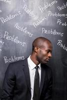 Problems all around me. Depressed African man in formalwear standing against blackboard with inscription Problems photo