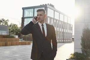 Confident mature businessman talking on mobile phone while walking near office building